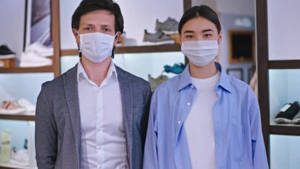 Portrait of a man and woman multiethnic with a protective mask in a shoe shop in front of the camera looking straight in the pandemic of Coronavirus — Stock Video