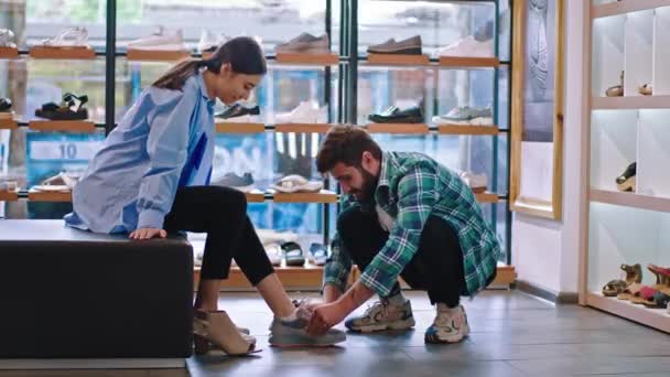 魅力的で笑みを浮かべて大規模な女性と彼女のボーイフレンドの靴店では、男は彼のガールフレンドに靴のペアを着用するのに役立つショッピング日があります。ARRIアレクサミニで撮影 — ストック動画