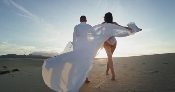 У літній день романтична і сексуальна пара, що ходить перед камерою, тримає довге плаття, яке вони відчувають дуже розслабленим — стокове відео