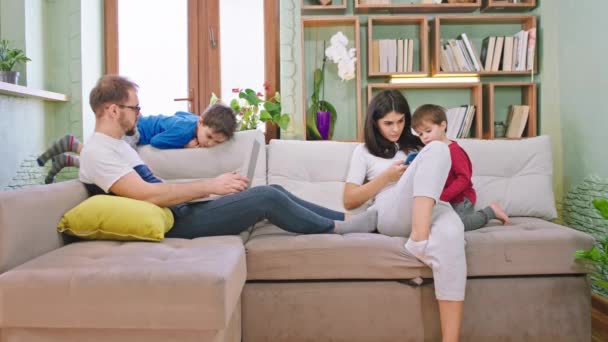 Di sofa di rumah keluarga menghabiskan waktu bersama ibu mengetik sesuatu di smartphone anak-anak bermain ayah berbaring di sofa — Stok Video