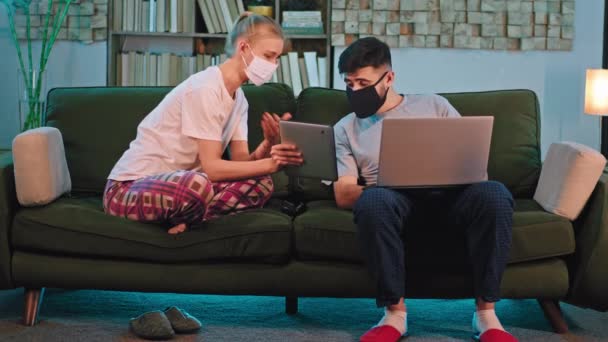 Bom tempo juntos passar um casal em casa em quarentena eles fazem algumas compras on-line senhora mostrando algo no tablet para seu parceiro enquanto ele está trabalhando no laptop — Vídeo de Stock