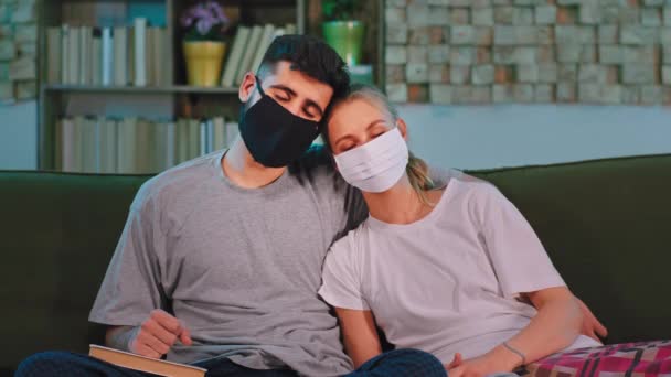 슬픈 커플 이 소파에 앉아 코로나 바이러스 (Coronavirus) 라는 전염병에서 보호 마스크를 쓰고 눈을 감고 있습니다. — 비디오