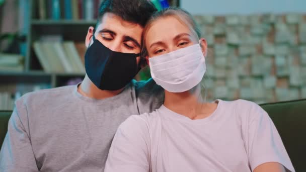 Daheim im Wohnzimmer vor der Kamera bleibt das Paar mit Schutzmaske und traurigem Blick in die Kamera in Quarantäne des Coronavirus — Stockvideo