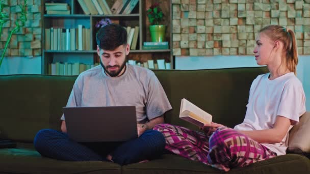 Em casa na sala de estar casal jovens estudantes ficar no sofá estudando o acabamento para estudar e começar a assistir a TV na frente da câmera. Tiro em ARRI Alexa Mini — Vídeo de Stock