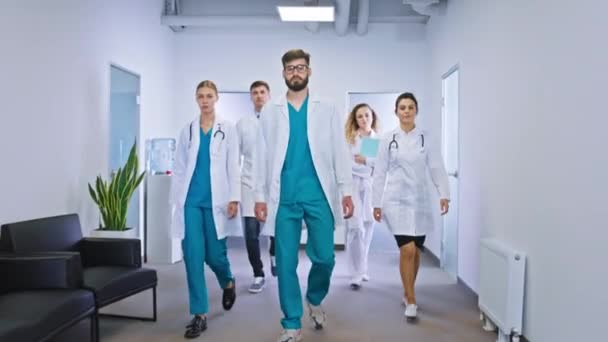 У великій лікарні сучасний коридор, що йде перед групою камери і медсестер вони зупиняються і дивляться на камеру — стокове відео
