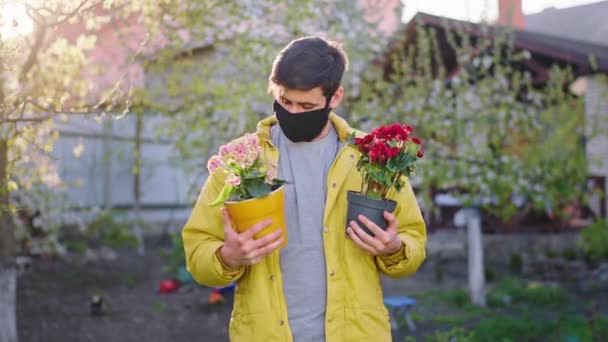 Snygg man i trädgården som håller två blomkrukor och känner sig väldigt glad att han tar hand om blommorna i denna pandemi av Coronavirus 2019 — Stockvideo