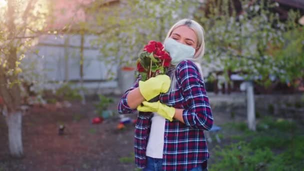 Charismatická blondýnka na zahradě doma si užívá čas, kdy se dívá přímo do kamery s ochrannou maskou v karanténě Coronavirus 2019 — Stock video