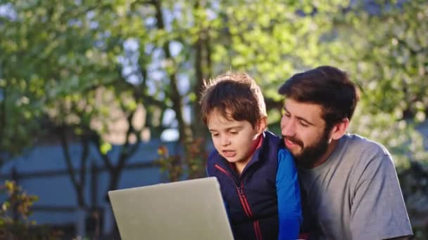 Perfecto día soleado papá y su lindo hijo pequeño se quedan en casa en el jardín y charlando juntos pasan un buen rato usando la tableta para jugar un juego — Vídeo de stock