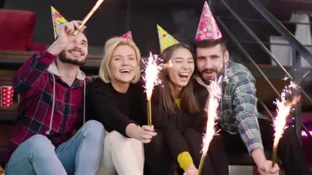 Bei giovani che festeggiano la festa di compleanno dopo aver finito il college in biblioteca usando la scintilla e hanno il cappello di compleanno guardano dritto alla fotocamera — Video Stock