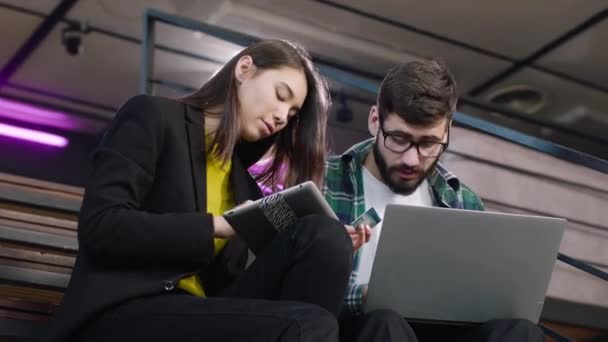 Feliz y carismático dos estudiantes multiétnicos pedir algo en línea utilizando una tarjeta de crédito y tableta electrónica primer plano de la cámara — Vídeos de Stock