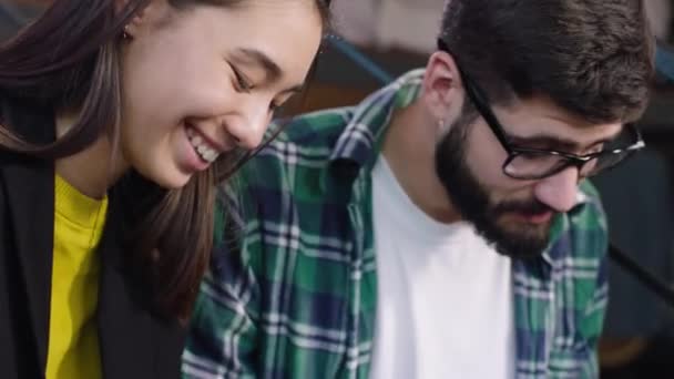 Sorrindo grande cara carismático e jovem senhora japonesa encomendar algo on-line a partir do cartão de crédito usando um tablet eletrônico eles sentados nas escadas da biblioteca — Vídeo de Stock