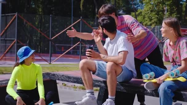 Wanita cantik dan dua pria multietnis sangat tampan memiliki pertemuan di taman skateboard perkotaan mereka duduk di lantai dan di kursi taman mereka membahas antusias sambil memegang skateboard. Ditembak — Stok Video