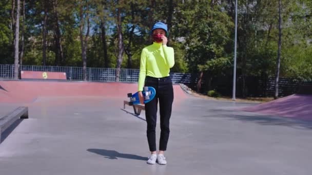 Coronavirus tijd mooie dame in het midden van moderne skate park staan in de voorkant van de camera met een beschermend masker ze gelukkig af te nemen van het masker en lachen grote — Stockvideo