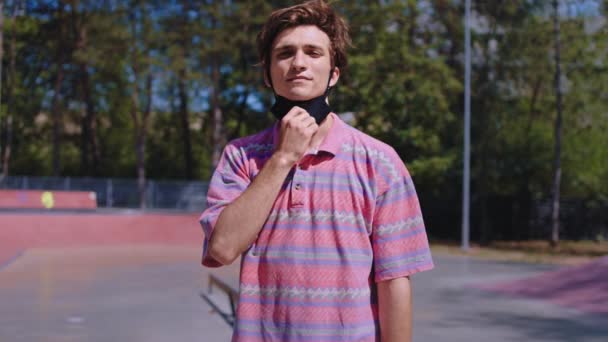 Coronavirus tiempo chico guapo en un parque de skate urbano quitarse la máscara delante de la cámara y sonriendo a lo grande que se siente feliz — Vídeos de Stock