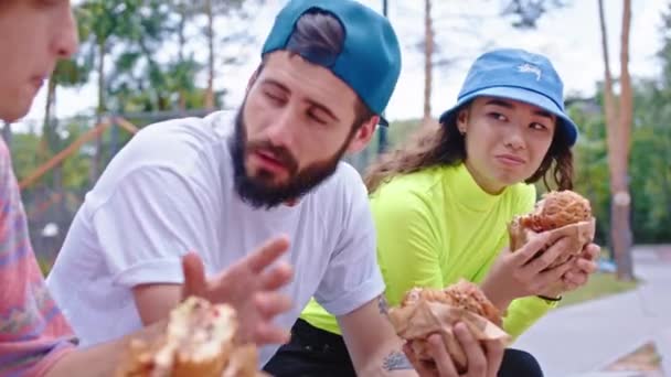 Oběd čas v městském skate parku detailní up k fotoaparátu multietnické skupiny dospívajících lidí těší rychlé občerstvení v přírodě — Stock video