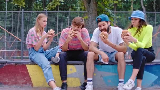 Giornata di sole nel bel mezzo di skate park amici multietnici hanno un tempo di pausa si prendono il pranzo nel bel mezzo del parco mangiare qualche hamburger — Video Stock