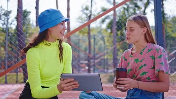 Primer plano delante de la cámara dos buenas amigas disfrutando del tiempo fuera en el parque viendo algo en la tableta electrónica y analizando juntas algunas ideas — Vídeo de stock