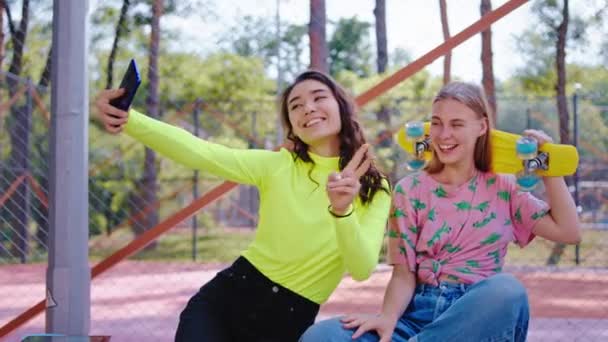 En un parque de skate urbano, dos carismáticos con una gran sonrisa, las señoras se toman unos selfies con el smartphone que posan frente a la cámara, toman algunas fotos para recordar a la rubia que sostiene el... — Vídeos de Stock