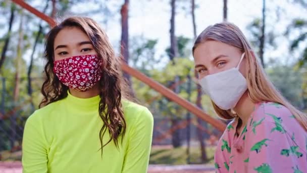 Delante de la cámara retrato de damas con máscara protectora mirando directamente a la cámara en un moderno parque callejero en pandemia de Coronavirus. 4k — Vídeos de Stock