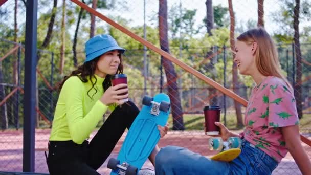 Nowoczesny styl życia Dwie młode kobiety dyskutują w nowoczesnym skateparku robią sobie przerwę po ciężkiej jeździe z deskorolką pijącą kawę — Wideo stockowe