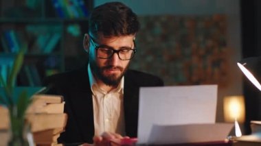Gözlüklü karizmatik bir adam dizüstü bilgisayarında bir şeyler yazıyor. Kütüphanede online kursuna çalışıyor.