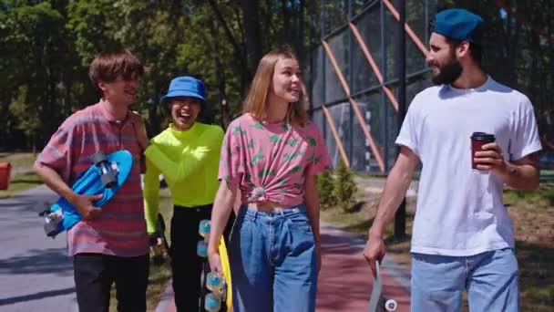 Marcher groupe excité d'amis avec un grand sourire ils tenant le skateboard à côté d'un skate park moderne ils socialisent ensemble. Tourné sur ARRI Alexa Mini — Video