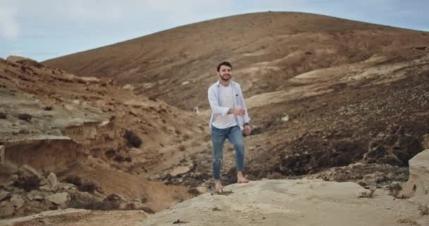 Ung kille med ett stort leende mycket attraktiv entusiastisk resa ensam genom klipporna och stranden — Stockvideo