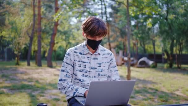 Charismatische Student nehmen den Laptop in der Pandemie und studieren im Park trägt er Schutzmaske in der Pandemie des Coronavirus — Stockvideo