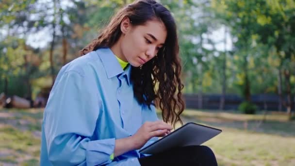 V parku asijské dáma s dlouhými vlasy pomocí elektronického tabletu na společenský s někým velmi koncentrované, zatímco se trochu čerstvého vzduchu — Stock video
