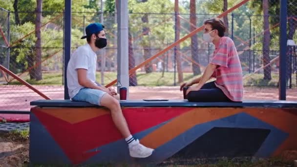 Chicos atractivos en el parque con una máscara protectora en la cara discutiendo juntos respetan una distancia social en la pandemia de Coronavirus — Vídeo de stock