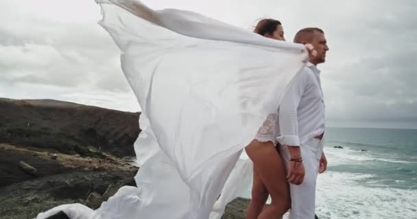 Beyaz elbiseli romantik genç çift birbirlerine sarılıyorlar rahat ve coşkulu hissediyorlar. — Stok video