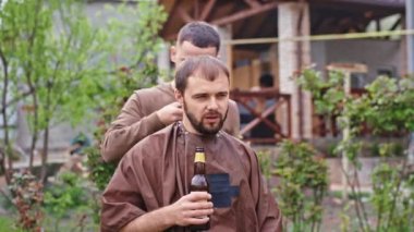 Evdeki adam berberle sohbet ederken saçlarını kesmeye hazırlanırken elinde bir şişe bira tutuyordu.