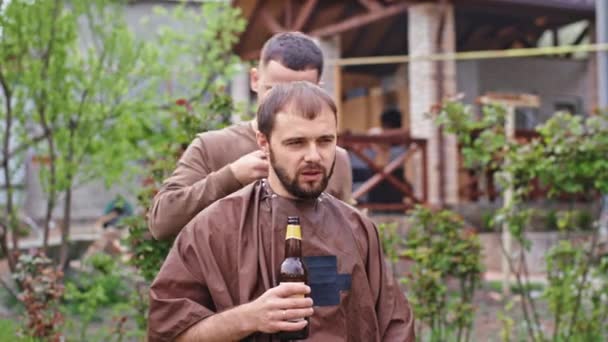 À la maison l'homme bavarder avec le coiffeur tout en se préparant à faire une coupe de cheveux il tenant une bouteille de bière — Video