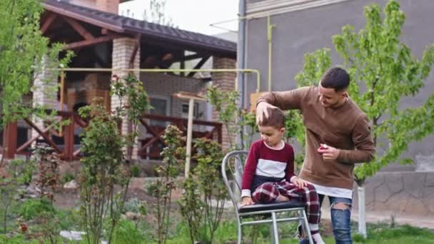 Bel bambino hanno un taglio di capelli fatto in giardino l'uomo barbiere professionista finire il taglio di capelli prendere un po 'di polvere di capelli e finire il taglio di capelli — Video Stock