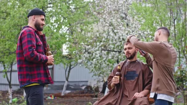 Kameranın önünde karizmatik bir adam bahçede arkadaşlarıyla sohbet ediyor. Onlar bira içerken, o profesyonel bir berberle saç kesimi yapıyor. — Stok video