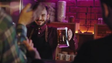 Modern bir bardaki karizmatik gülümseyen büyük barmen bar masasındaki müşterisine bira veriyor. Çok heyecanlı ve mutlular.