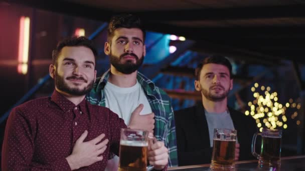 Les gars attrayants dans un bar sportif regarder concentré et très émotionnel la finale du jeu de leur équipe fav devant la télévision tout en buvant de la bière. 4k — Video