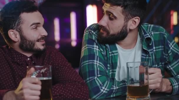 Dobrze wyglądający faceci przed kamerą, siedzący w pubie, pijący piwo, rozmawiający i oglądający mecz foo, bardzo emocjonujący, świetnie się bawią. — Wideo stockowe