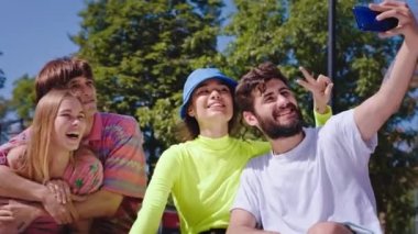 Kameranın önünde parktaki iki çift modern akıllı telefon kullanarak selfie çekiyorlar ve dışarıda eğleniyorlar.