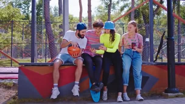 Beau jeune groupe d'amis élégants profiter du temps ensemble au milieu du parc moderne, ils socialiser ensemble l'un des gars jouent avec un basket-ball. Tourné sur ARRI Alexa Mini — Video