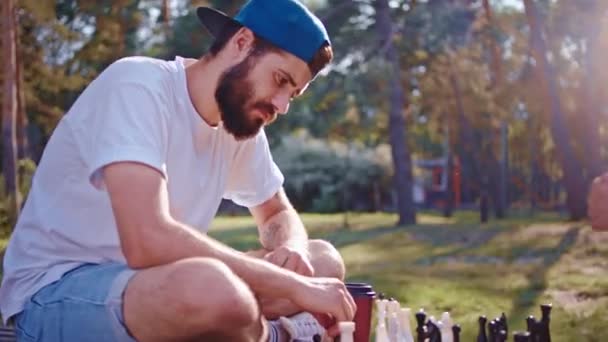 Temiz havada yakışıklı bir adam ve arkadaşı büyük modern parkta satranç oynuyorlar. 4k — Stok video