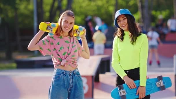 Duas amigas senhoras multiétnicas no meio do moderno parque de skate em pé na frente da câmera e sorrindo grande eles segurando o skate se preparar para um passeio — Vídeo de Stock