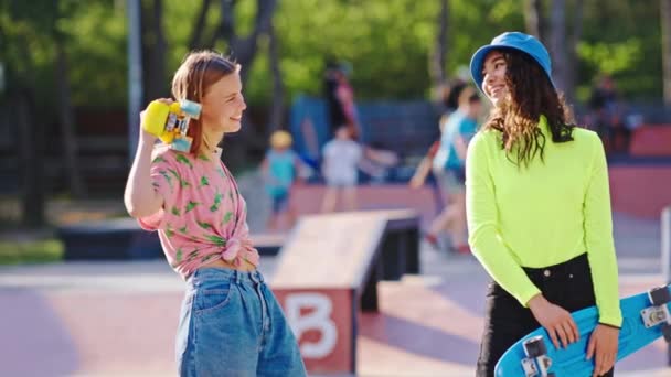 Increíble aspecto de las mujeres jóvenes sonriendo grandes pasar tiempo juntos en un moderno parque de skate en frente de la cámara que sostiene el monopatín en las manos — Vídeo de stock