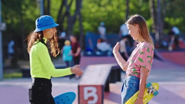 Słoneczny dzień w miejskim skateparku dwie charyzmatyczne damy spotykają się w parku zabierają deskorolkę i wybierają się na przejażdżkę — Wideo stockowe