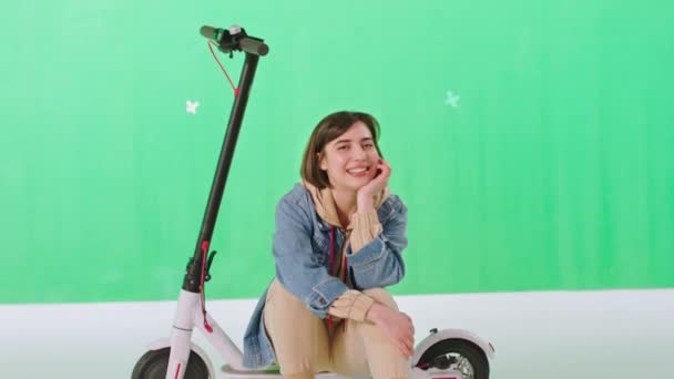 En un estudio de croma key mujer guapa con un pelo corto sentado en su scooter eléctrico y mirando directamente a la cámara y sonriendo bonita. Disparo en ARRI Alexa Mini — Vídeo de stock