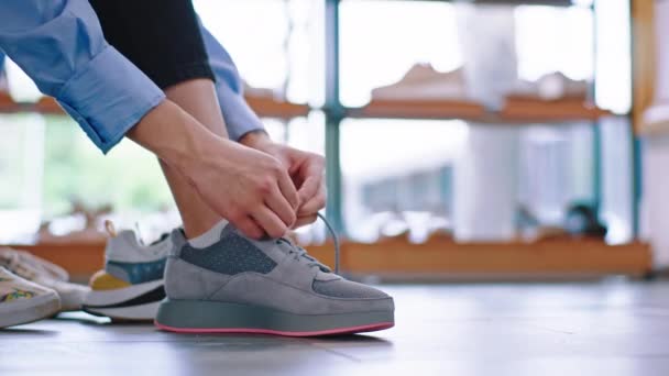 En una tienda de zapatos luminosa una señora se sienta en el sofá y trata de usar un nuevo par de zapatos deportivos — Vídeo de stock