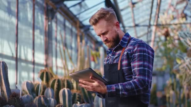 W rolniczym ogrodniku szklarni skoncentrowany sprawdzić listę roślin ozdobnych podczas korzystania z jego smart tablet — Wideo stockowe