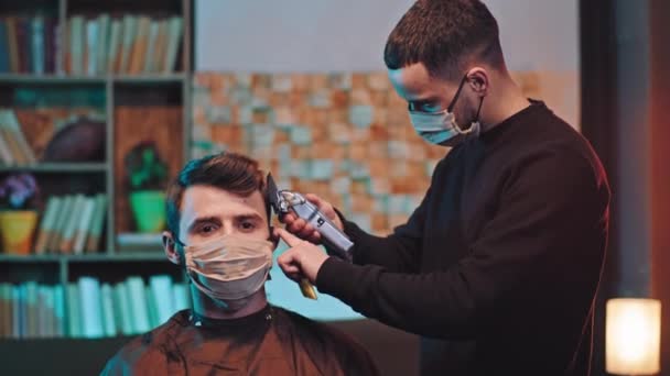 Nella quarantena in casa l'uomo concentrato seduto sulla sedia ha un parrucchiere taglio di capelli e l'uomo indossa maschera protettiva concetto di Coronavirus — Video Stock