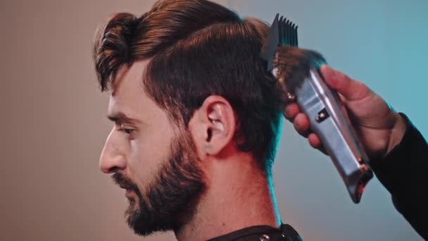 Homem bonito em uma barbearia tem um barbeiro de corte de cabelo profissional usando clipper profissional para fazer o corte feito — Vídeo de Stock