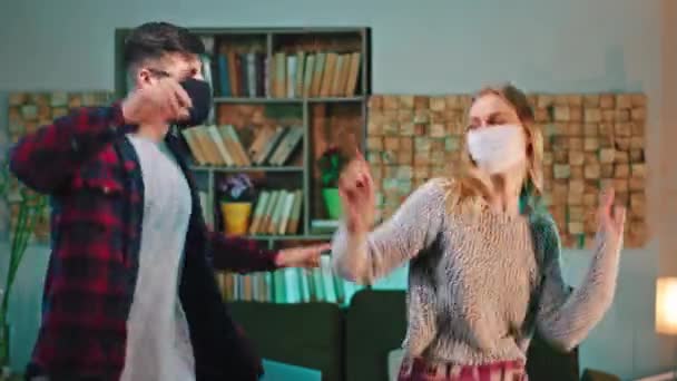 Dans la quarantaine à la maison couple charismatique en pyjama vêtements de maison dansant avec le concept de masque de protection de Coronavirus — Video